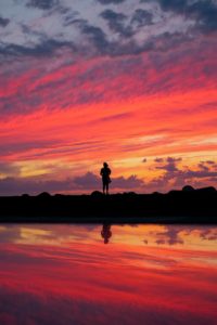 silhouette of man standing on seashore during sunset